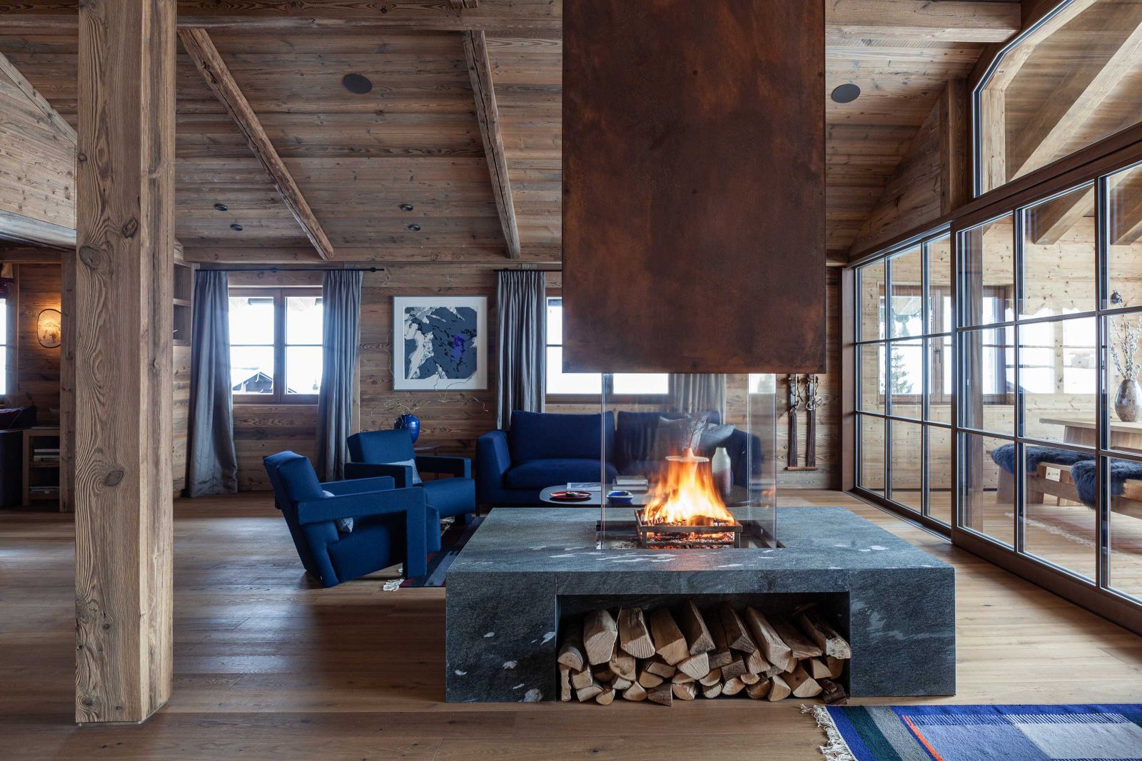 Der freistehende Kamin dominiert den offenen Wohnbereich und verleiht mit seinen flackernden Flammen dem Chalet eine wohlige Atmosphäre. Sessel im Vordergrund: «Utrecht» von Gerrit Rietveld, ursprünglich entworfen für das Kaufhaus Metz & Co in Amsterdam, Redesign Cassina.