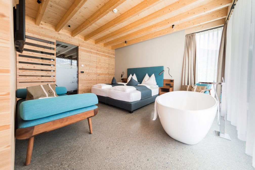 44 Zimmer zählt das Hotel, daneben auch zwei etwas abgelegenere Chalets mit eigener Sauna, die den perfekten Rückzugsort bieten. Der Grossteil des Interieurs ist aus heller, heimischer Lerche gefertigt, im Kontrast dazu der grünstichige Terrazzo-Boden. Sitzmöbel von Artisan aus dunklem Walnussholz und Textilbezügen in Petrol runden das Gesamtbild harmonisch ab.