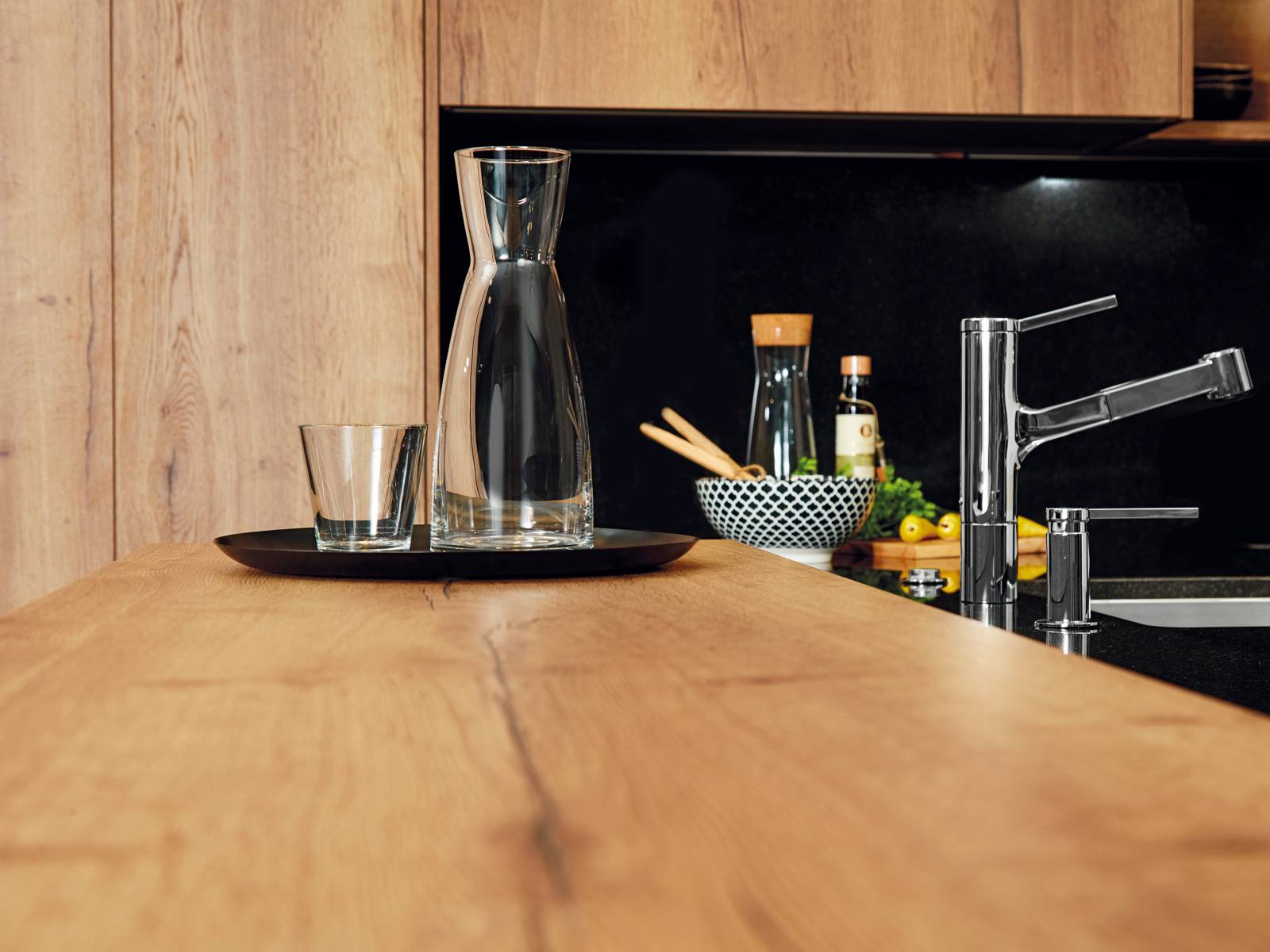 Elemente in Holzoptik erzeugen zusammen mit der eleganten Granitabdeckung eine moderne Herzlichkeit, die zum Ankommen und Verweilen einlädt. Diese Materialkombination ist bezeichnend für die Küche Typ «hochmodern», deren technisches Highlight ein Kochfeld mit intelligenter Dunstabzugshaube ist, die per Handy oder Tablet gesteuert werden kann. Sabag.