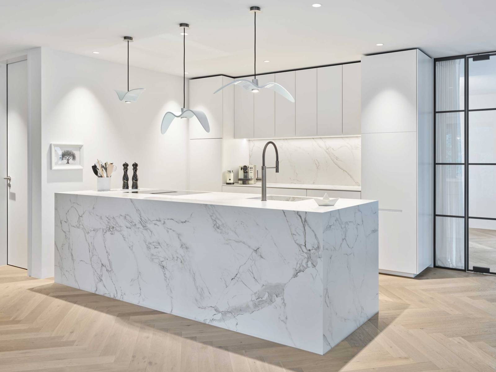 So wenig Küche wie möglich bei maximaler Wirkung: Alle Geräte sind hinter den reinweissen Fronten verborgen und stören den skulpturalen Charakter nicht. Der Inselblock ist ganz und gar in Dekton mit Marmoroptik gekleidet, was dem offenen Raum viel Eleganz verleiht und zum Industrial Look der Wohnung passt. STUBER TEAM.